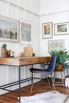 a desk with some plants and pictures on the wall above it, along with a chair