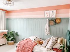 a bedroom with pink and green walls, white bedding and plants on the wall