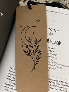 a bookmark with an image of a plant and the moon on it sitting next to some books