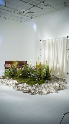 a bench sitting on top of a lush green field next to a white wall and drapes