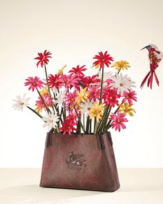 a vase filled with lots of flowers on top of a white table next to a bird