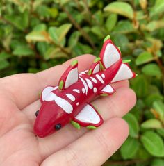 a hand holding a red and white toy with green leaves in the backgroud