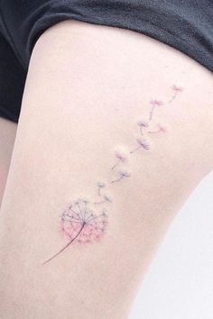 a woman's thigh with a small dandelion tattoo on her left side