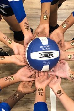 a group of people holding a volleyball in the middle of a circle with their hands on top of each other