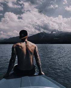 a man sitting on the back of a boat looking out over water with mountains in the background