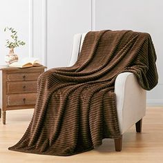 a brown blanket sitting on top of a white chair next to a wooden table and dresser