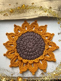 an orange and brown crocheted sunflower on a white surface with gold glitters