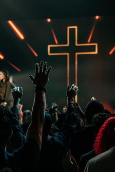 people raising their hands up in front of a cross on a stage with bright lights