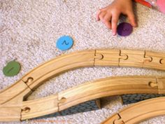 a child playing with wooden train tracks and matching numbers on the floor in front of them