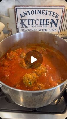 a pot filled with meatballs and sauce on top of a stove next to a sign