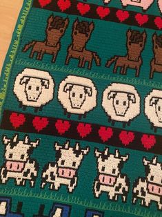 a knitted blanket with animals and hearts on it, sitting on a wooden table