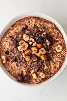 a bowl of oatmeal with nuts and raisins in it on a white surface