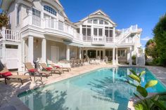 a large white house with a swimming pool in the front yard and deck chairs around it