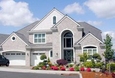 a car is parked in front of a house with flowers and shrubs on the driveway