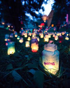 many lit up mason jars sitting in the grass with paper lanterns on top of them