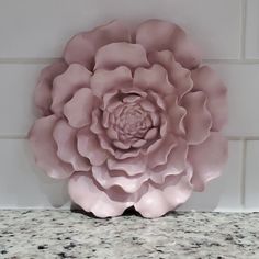 a large pink flower sitting on top of a counter next to a white tile wall