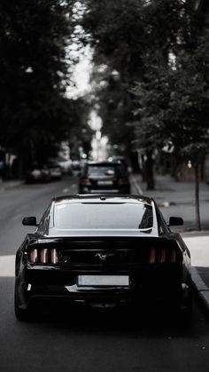 a black car parked on the side of a road next to trees and buildings with no people