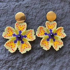 a pair of yellow and purple beaded flower earrings on top of a gray surface