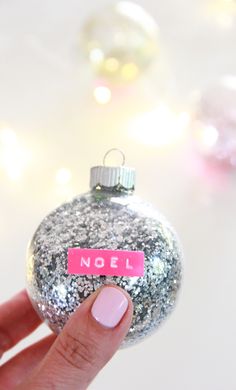 a hand holding a glittered ornament with a pink name tag on it