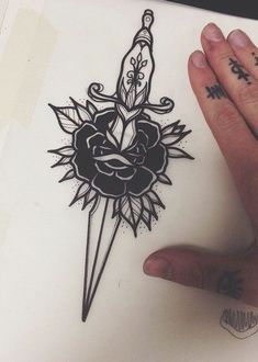 a hand holding a tattoo with a dagger and rose on it