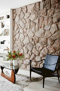 a living room filled with furniture and a stone wall behind the chair is a glass coffee table