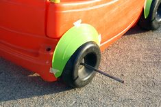 an orange and green wagon with wheels on the ground next to another vehicle's tire