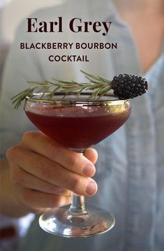 a person holding a wine glass with a blackberry bourbon cocktail in it and text overlay that reads, ear grey blackberry bourbon cocktail