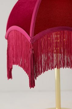 a pink table lamp with fringes on the top and bottom, against a white background