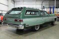 an old green station wagon is parked in a garage next to other cars and trucks