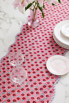 pink flowers are in a vase on a table with white plates and glassware next to it