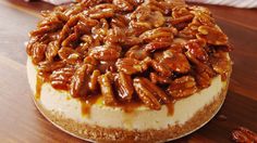 there is a cheesecake covered in pecans on top of a wooden table,