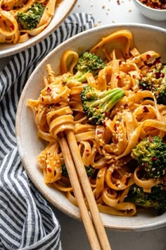 two bowls filled with noodles and broccoli next to chopsticks on a table