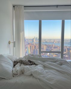 an unmade bed in front of a large window with the view of new york city