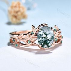 a ring with an oval green stone surrounded by leaves and flowers on top of a white surface