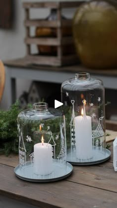 two glass candles sitting on top of a wooden table next to boxes with christmas decorations