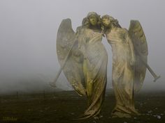 two angel statues standing in the middle of a foggy field with their arms around each other