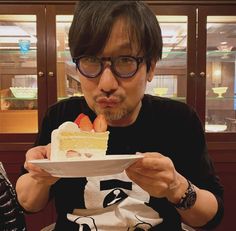 a man holding a plate with a piece of cake on it in front of his face