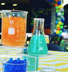 two beakles filled with blue and orange liquid sitting on top of a table covered in balloons