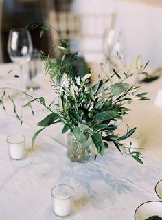 the table is set with candles and vases filled with flowers, greenery, and glassware