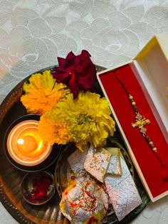 an assortment of flowers and candles on a tray with a candle in the middle,