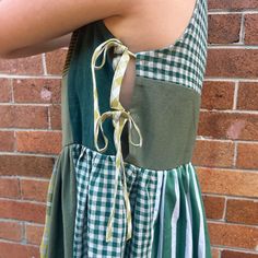 a woman wearing a green and white gingham dress standing in front of a brick wall