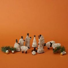 several small figurines made out of sticks and yarn on an orange background with pine needles