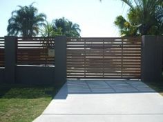 a gated driveway with grass and palm trees in the background