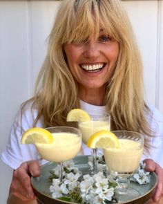 a woman holding two glasses with lemonade in them and flowers on the rims