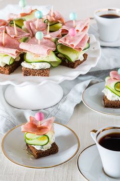 small sandwiches with cucumbers, ham and cream cheese on them next to cups of coffee