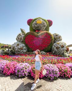 a woman standing in front of a large teddy bear made out of flowers and plants