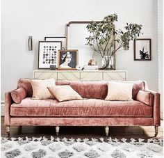 a living room with a pink velvet couch and some framed pictures on the wall above it