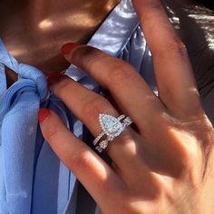 a woman's hand with a diamond ring on her left hand and a blue shirt