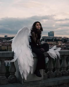 a woman with white wings sitting on a ledge