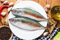 two fish sitting on top of a white plate next to some spices and pepper shakers